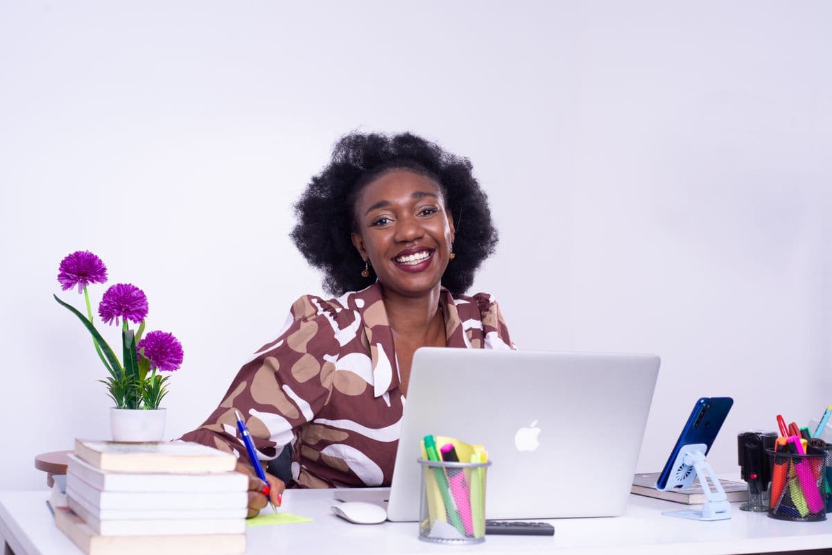 Jeune femme souriante à son bureau avec un ordinateur portable, illustrant le poste d’Assistant Executive Shopify chez a6ko.